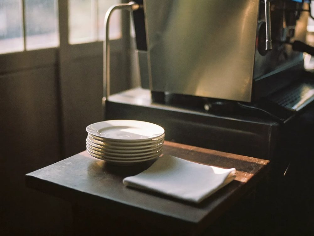Counter detail at The Grid Cafe: stacked saucers and a milk jug in window light